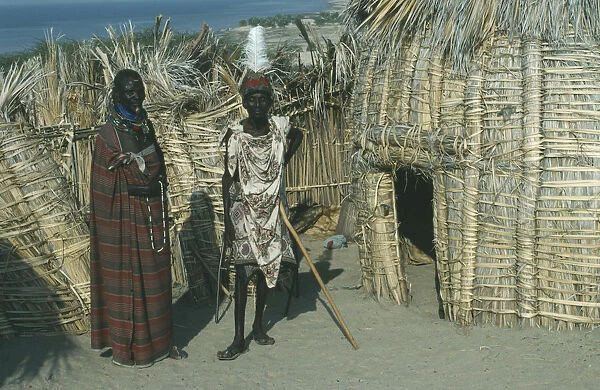 20069594. KENYA Lake Turkana Turkana tribe two men standing outside a traditional hut made
