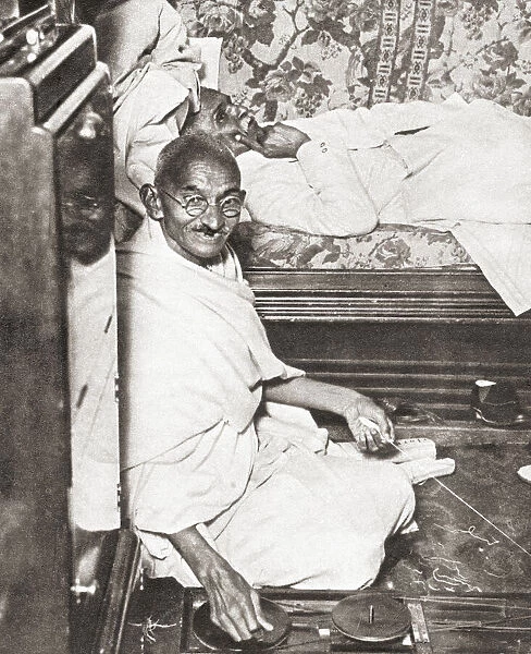 Mohandas Karamchand Gandhi, aka Mahatma Gandhi, 1869 - 1948. Indian activist, leader of the Indian independence movement against British rule. Seen here at the Round Table Conference, 1931. On the floor beside him is his spinning wheel, a symbol of his attempt to resurrect Indian industry at the expense of British trade. From The Pageant of the Century, published 1934