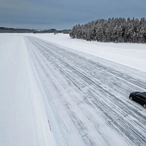 Car traveling on ice track on a frozen lake in the snow covered landscape, Jokkmokk, Norrbotten, Lapland, Sweden, Scaninavia, Europe