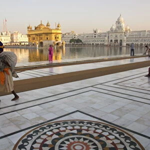 Elderly Sikh pilgrim with bundle and stick walking around holy pool