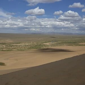View down a huge sand dune towards a ger dotted plain and distant hills on a summer evening