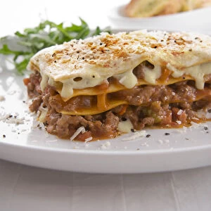 Traditional lasagne made with beef, pancetta and vegetables, served with rocket and bread, close-up
