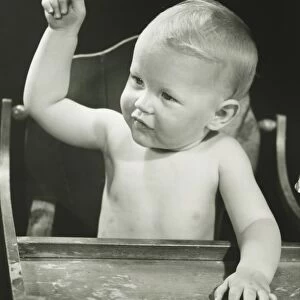 Baby boy (6-12 months) pointing, sitting in high chair, (B&W), portrait