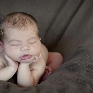 Newborn baby, five days, asleep with head propped up on hands