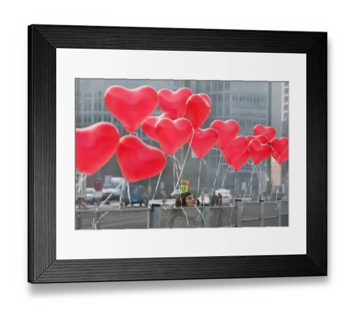 Framed Print : A woman fixes red heart-shaped balloons on a fence on Februray 14, 2012 in Berlin