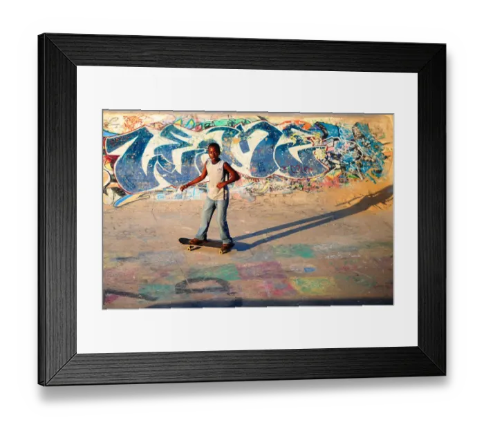 Framed Print : A young boy skateboards past a ramp decorated with graffiti in a skate park in Durban Framed Print : A young boy skateboards past a ramp decorated with graffiti in a skate park in Durban