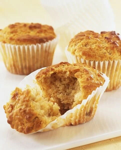 Three muffins in paper cases, muffin in forefront split open, revealing golden mixture
