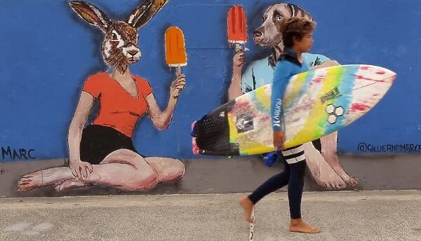 Australia-Lifestyle. A young surfer walks past street art on the way to