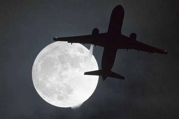 Britain-Supermoon. A plane flys in front of a 'super moon' or 'wolf moon'