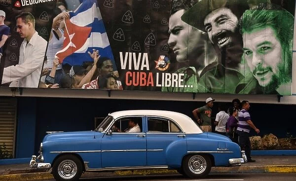 Cuba-Us-Feature-Car. An American classic car drives past a political poster
