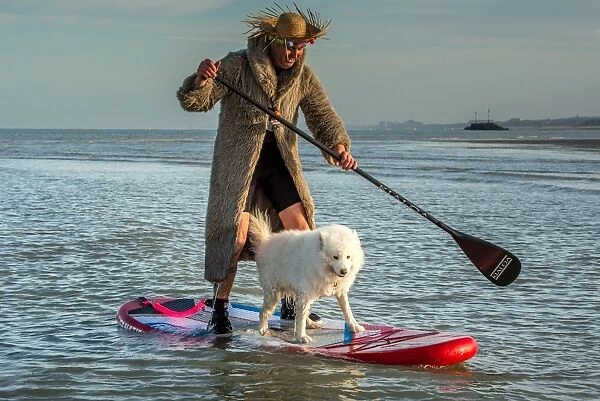 France-Surf-Dog. A man paddles with his dog on a surf board as people take