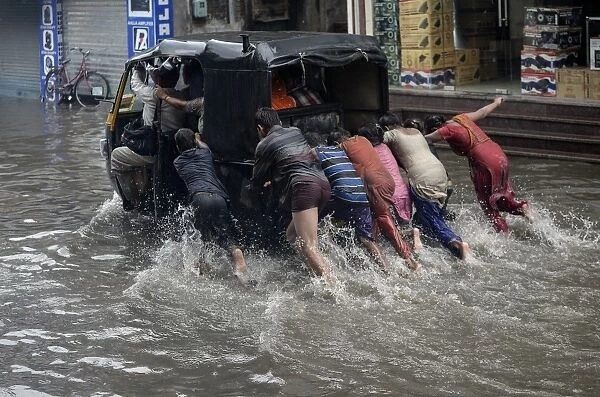 India-Weather-Rain. Indian children help to push an auto rickshaw along