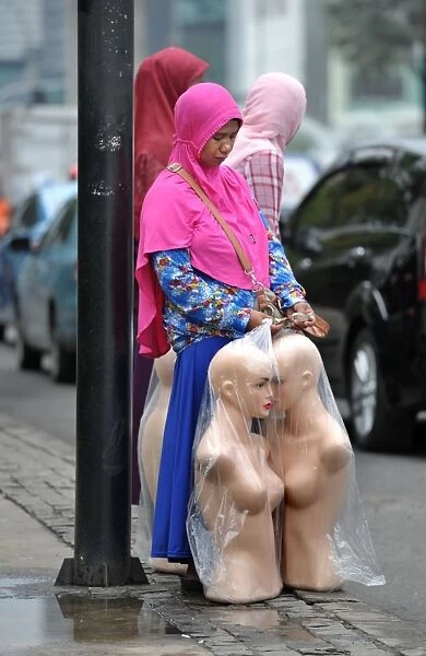 Indonesia-Economy. An Indonesian pedestrian holds mannequins as she waits