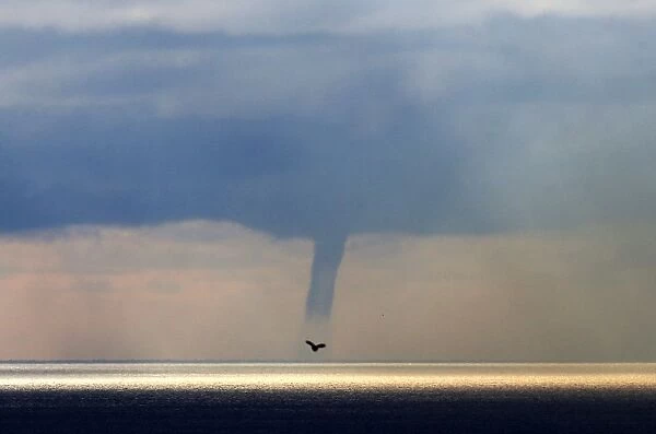 A waterspout forms on the horizon above the Mediterranean sea, off the coastal city