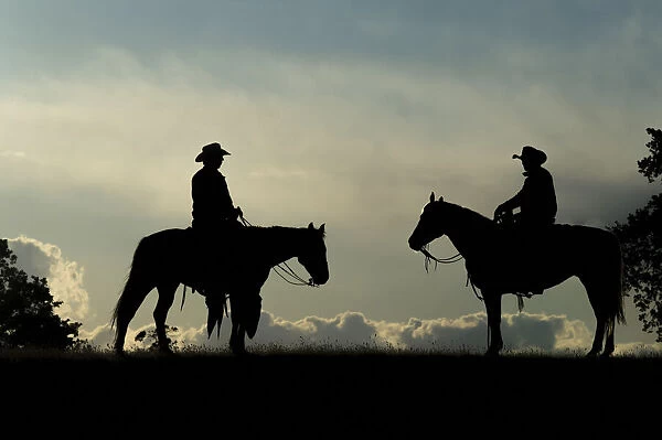 Silhouette of two cowboys on horses against a cloudy sky; Montana, United States of America