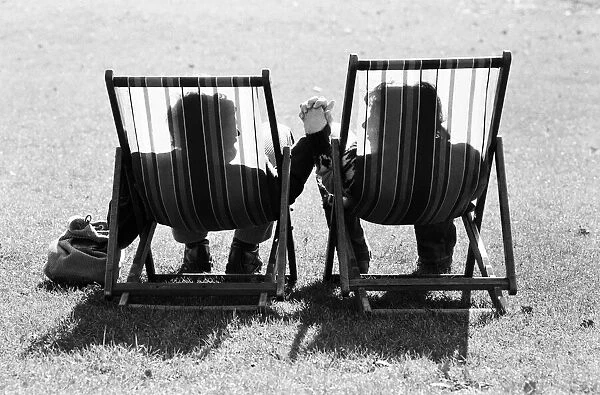 A couple in sit in a pair of deckchairs holding hands and looking at one another as they