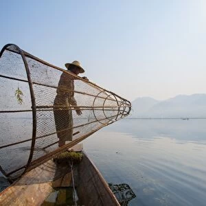 A basket fisherman on Inle Lake prepares to plunge his cone shaped net, Shan State