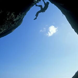 A climber ascending a cave archway at Foxhole, Gower Peninsula, Wales, United Kingdom