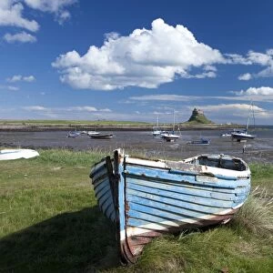 Old wooden fishing boat on a grassy bank with Lindisfarne harbour and Lindisfarne Castle in the background, Holy Island (Lindisfarne), Northumberland, England, United