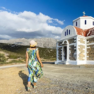 Rear view of woman in dress and straw hat walking to the Greek Orthodox church of Agia