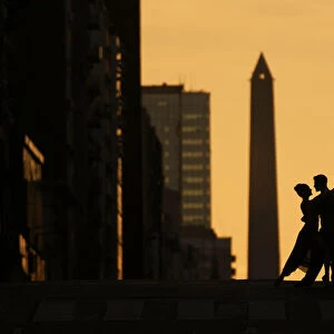 A couple of Professional Tango dancers on Avenida Corrientes at sunset, with the Obelisk monument in the background. Buenos Aires, Argentina. (MR)