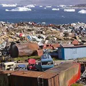 Rubbish dumped on the tundra outside Illulissat in Greenland with icebergs behind from the Sermeq Kujullaq or Illulissat Ice fjord. The Illulissat ice fjord is a Unesco world heritage