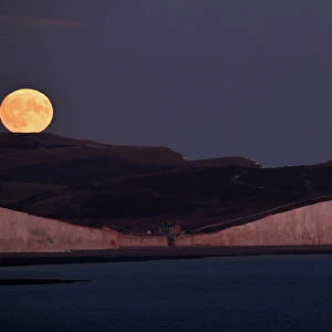 The moon is seen rising behind the Seven Sisters Cliffs at Birling Gap in East Sussex