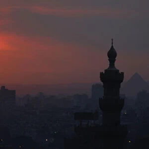 The sun sets on the minarets and the Great Pyramids of Giza in Old Cairo