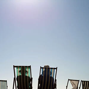 Sunbathers sit on deck chairs on Brighton beach, southern England