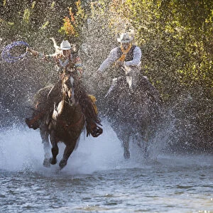 USA, Wyoming, Shell, The Hideout Ranch, Cowboy and Cowgirl on Horseback Running through the River