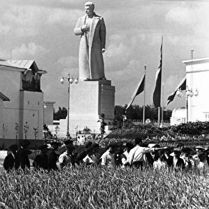 The all-union agricultural exhibition in moscow, august 1939, visitors to the exhibition examining specimens of a couch-grass / wheat hybrid (developed by member of the academy of sciences, tsitsin) at the demonstration field of the grain pavillion, in the background is a newly erected statue of stalin