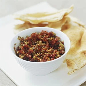 Bowl of tomato tapenade sauce served with crispy breads, close up