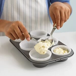 Boys hands spooning vanilla cake mixture into paper cases in a muffin tray