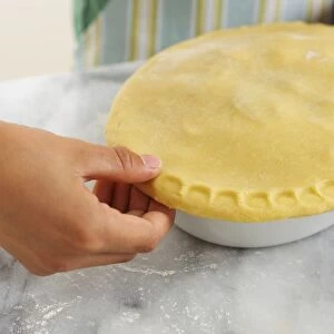 Girl using thumb to pressing edges of pastry lid on top of apple pie