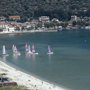 Greece, Ionian islands, Vasiliki, sailing boats with brightly coloured sails, white-sand beach, villas in background on hillside