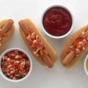 Hot dogs topped with tomato salsa, next to bowls of tomato ketchup, mustard, and tomato salsa