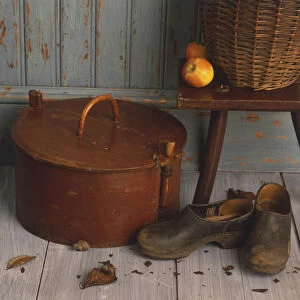 Wicker basket and apples on wooden stool, old cylindrical wooden box, soiled pair of shoes, front view