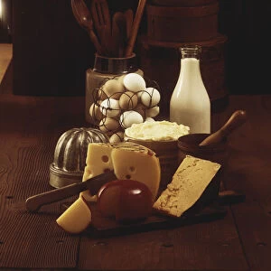 Cheese on wooden board with milk and eggs in background
