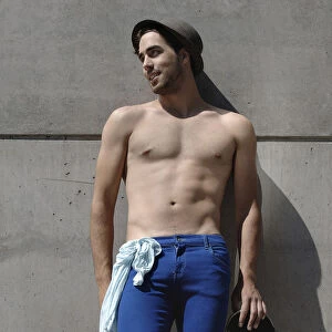 Young shirtless skater in front of a concrete wall