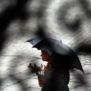 Photo taken through a metal gate shows an elderly woman shading herself from Photo taken through a metal gate shows an elderly woman shading herself from