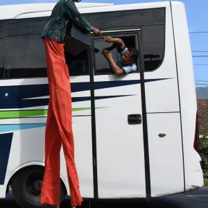 Print of a performer on stilts receiving money from a man on a bus in Indonesia Print of a performer on stilts receiving money from a man on a bus in Indonesia