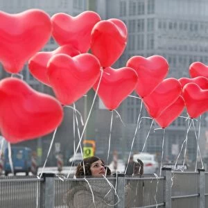 A woman fixes red heart-shaped balloons on a fence on Februray 14, 2012 in Berlin