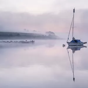 Sailing boat reflected in Wimbleball Lake in morning mist. Exmoor National Park, Somerset, England, UK. September 2020