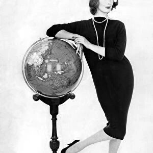 Woman wearing long dress poses leaning against a globe on a stand