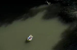 A Kosovo man lying in an inflatable boat takes a sunbath near a waterfall to cool