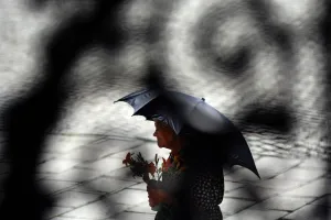 Photo taken through a metal gate shows an elderly woman shading herself from the Photo taken through a metal gate shows an elderly woman shading herself from the