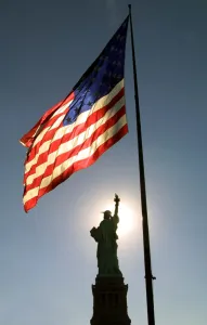 Prints of The Statue Of Liberty is silhouetted as the US flag waves as Liberty Island and Ellis Island, the immigration museum, reopened to the public for the first time. AFP PHOTO/Timothy A USA Prints: Us-Statue of Liberty